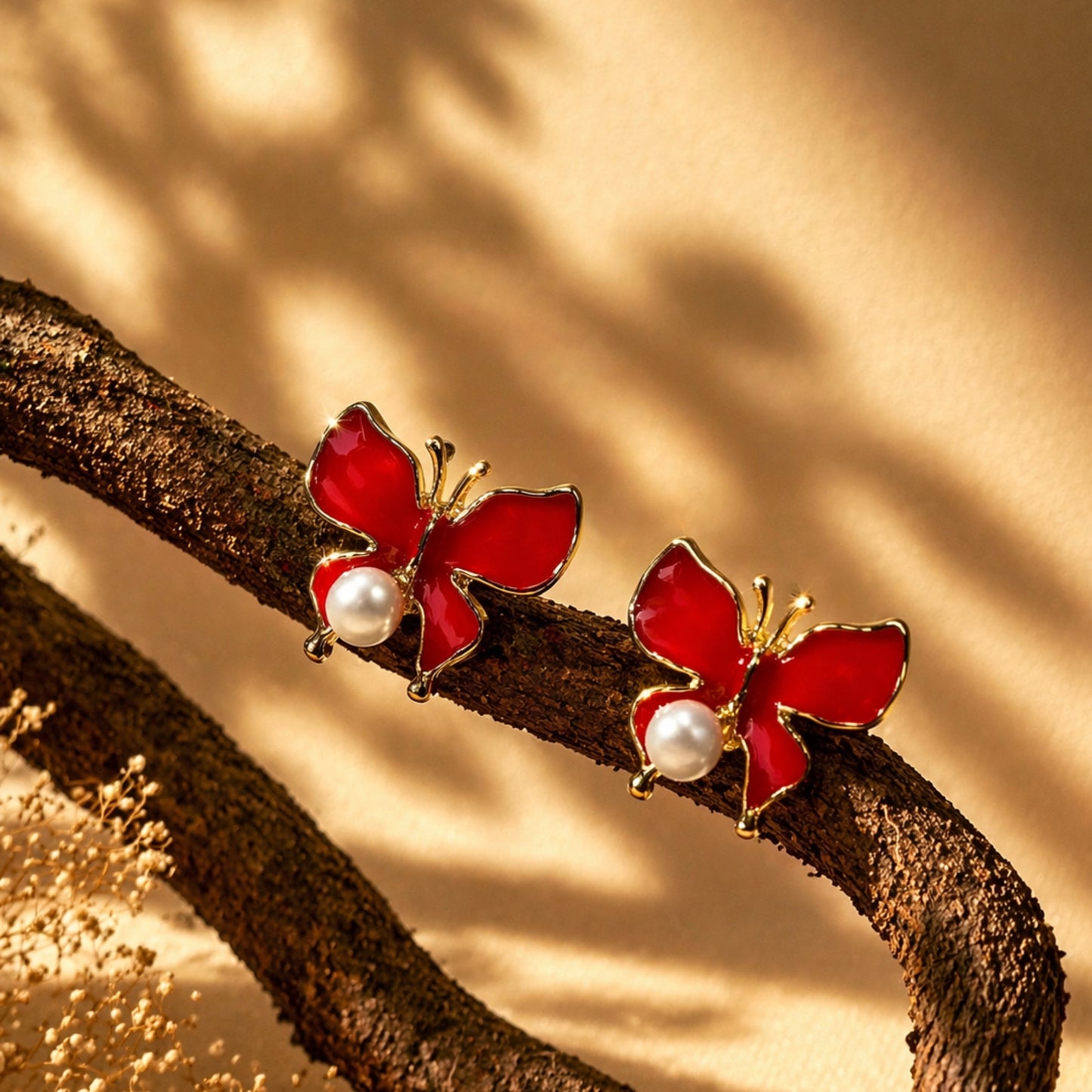 Red butterfly earrings with pearl centers on a branch against a warm background