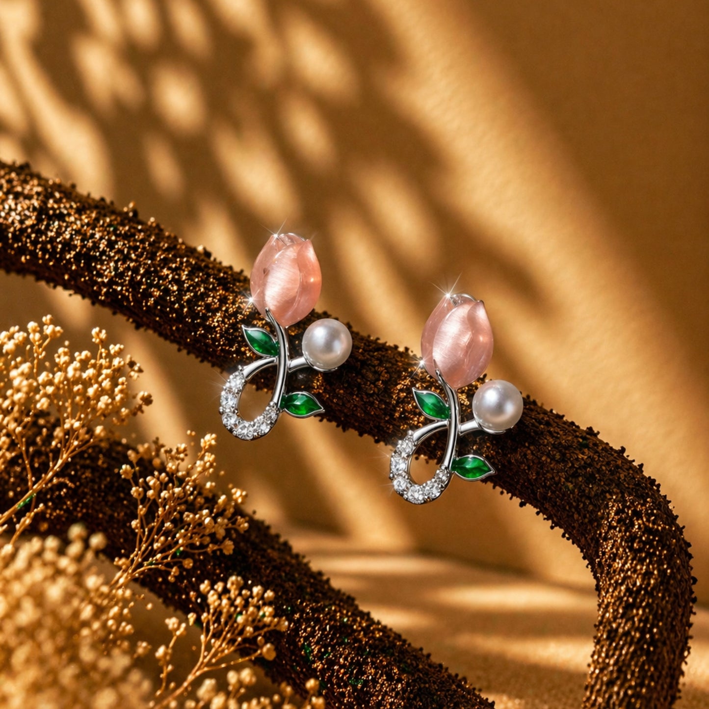 Pair of earrings with pink stones and green leaves on a textured brown surface.