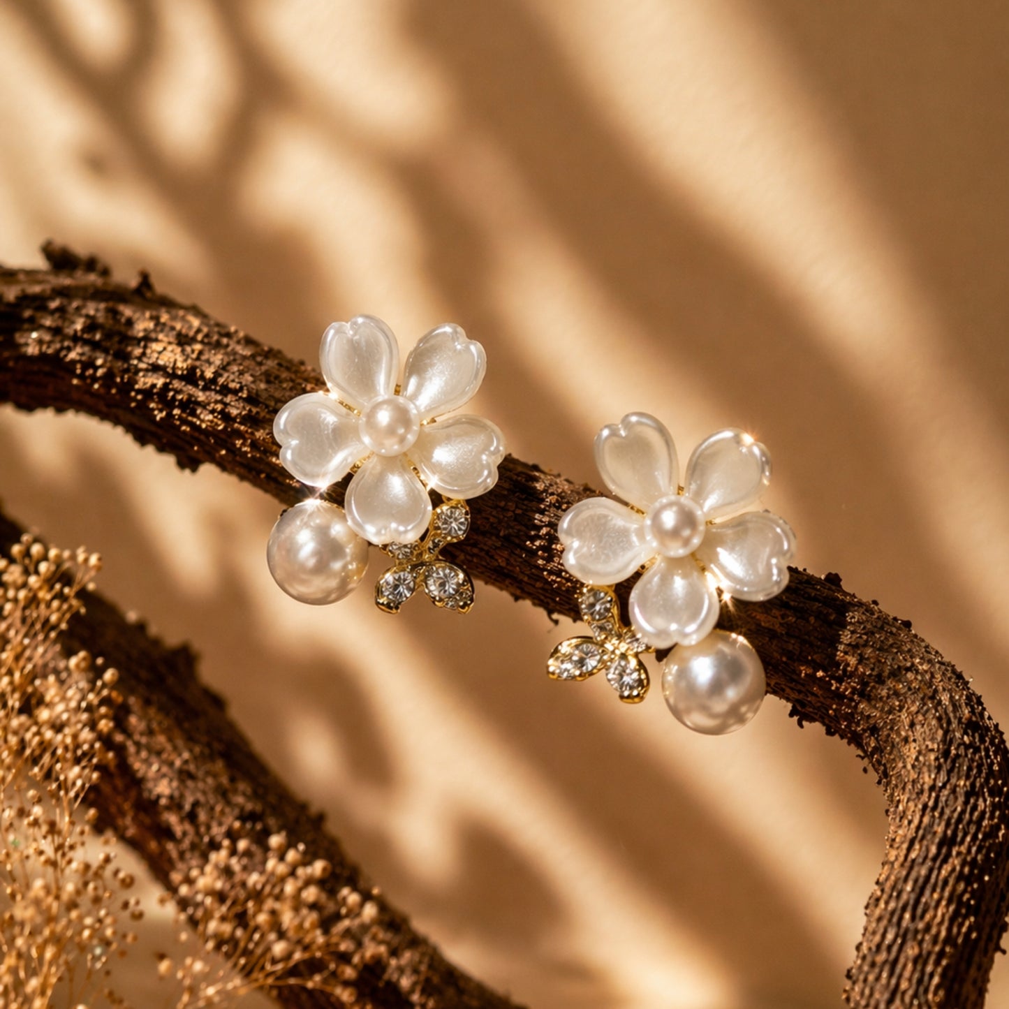 Flower-shaped earrings with pearls and crystals on a branch against a beige background